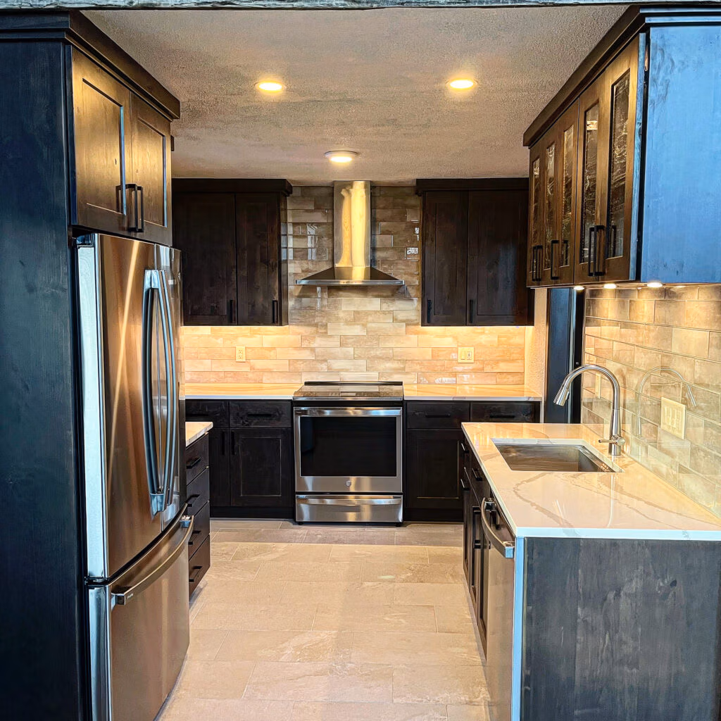 Modern kitchen interior featuring dark cabinetry, stainless steel appliances, quartz countertops, and warm lighting, showcasing a durable design suitable for mountain living in Summit County.