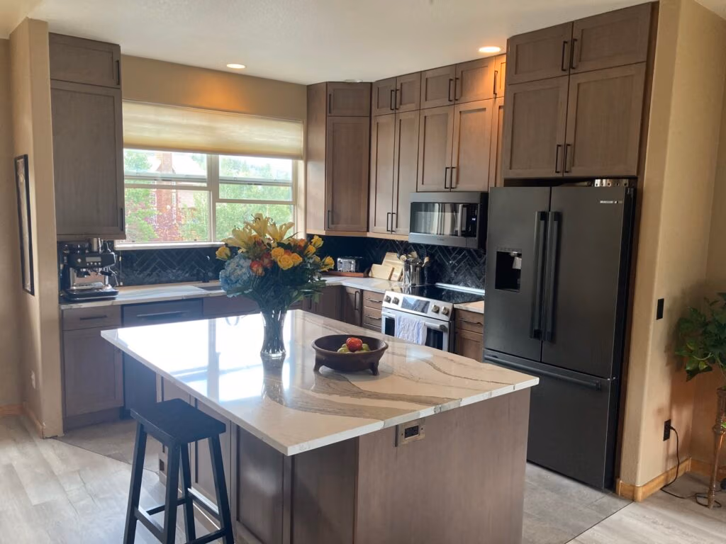 Modern kitchen with dark cabinetry, stainless steel appliances, and a central island featuring a flower vase and fruit bowl, showcasing a stylish and functional design suitable for mountain living in Summit County.