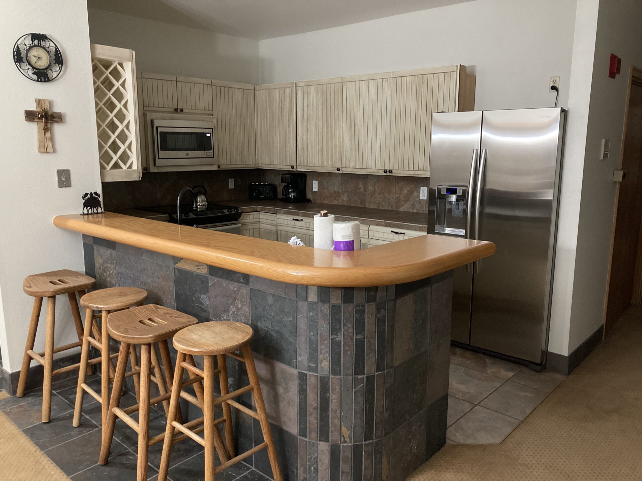 Breckenridge kitchen featuring wooden bar stools, stainless steel refrigerator, and rustic cabinetry, reflecting home remodeling aesthetics.