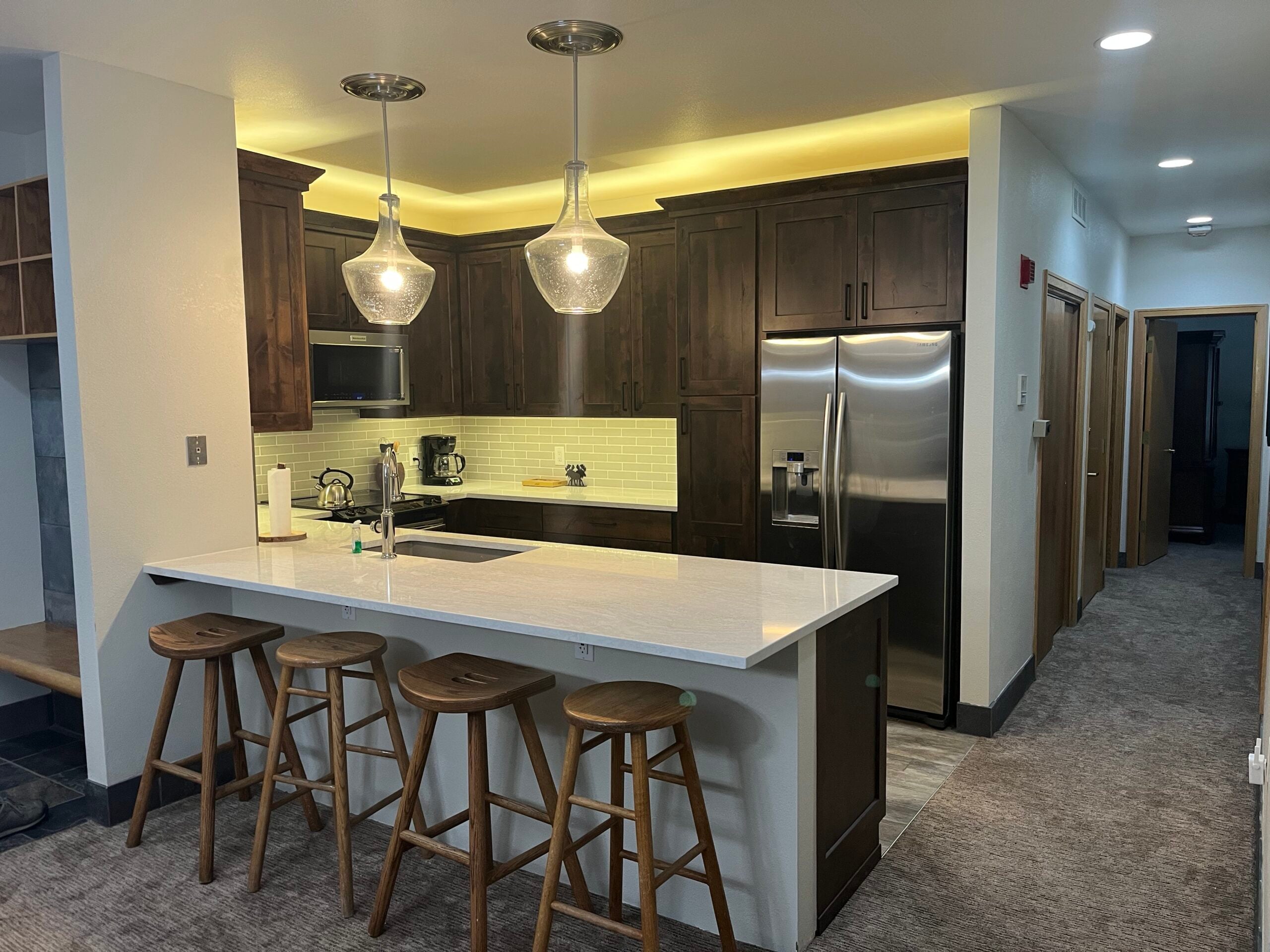 Modern kitchen with dark wooden cabinets, white countertops, pendant lighting, and bar stools, showcasing a stylish remodel in Summit County.