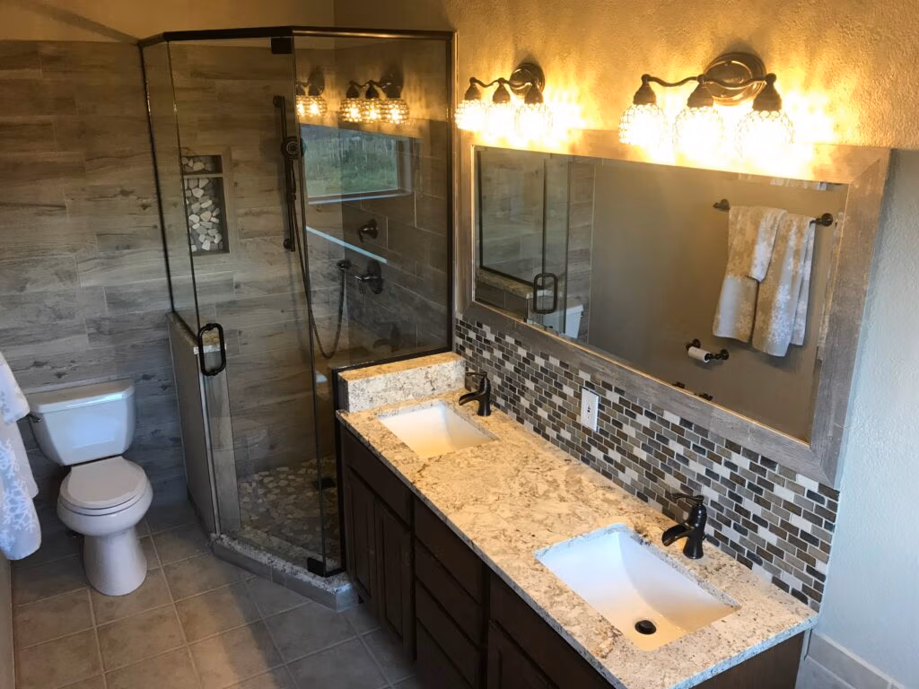 Modern bathroom with dual sinks, granite countertops, glass shower enclosure, and stylish lighting, showcasing remodeling features relevant to Natural Builders' services in Frisco, Colorado.