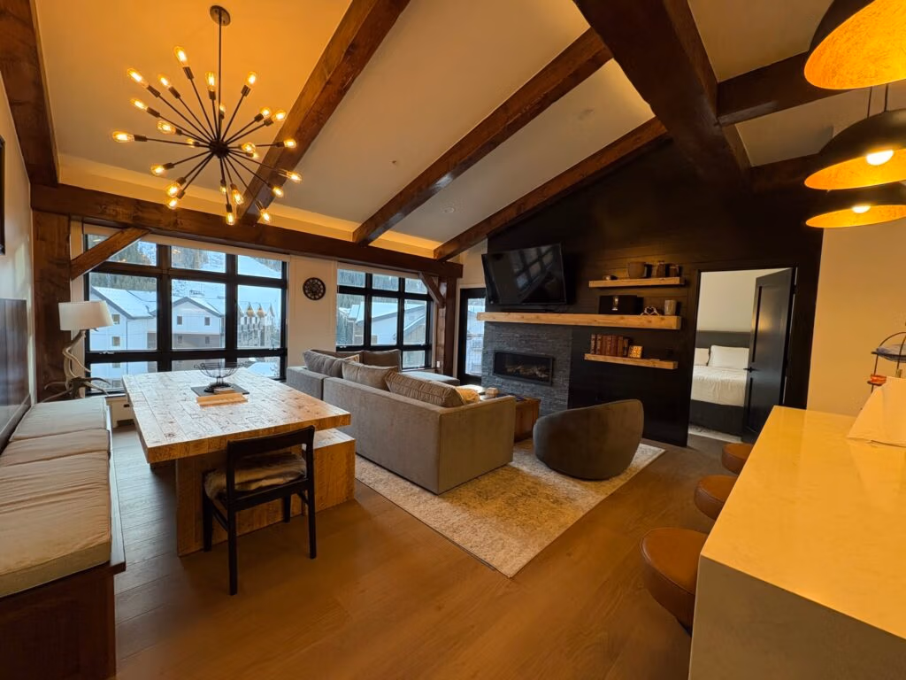 Modern living room and dining area with wooden beams, stylish furniture, and large windows showcasing a snowy landscape, emphasizing home remodeling and design.