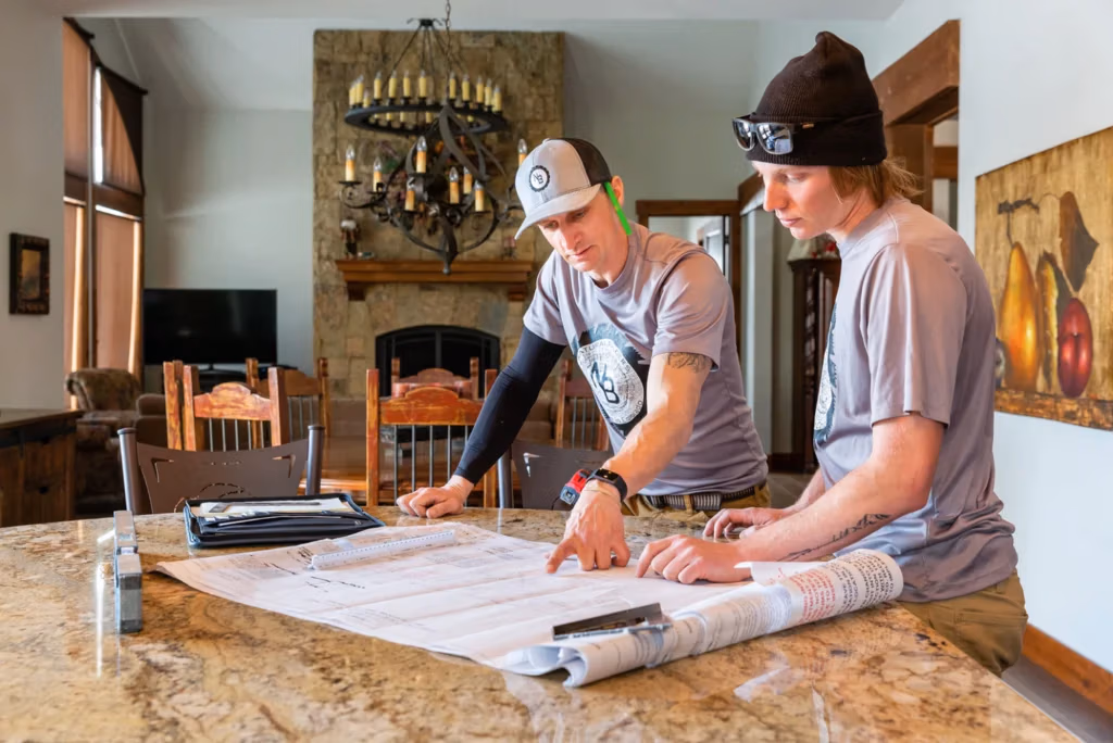 Two construction professionals reviewing project plans on a granite countertop in a home setting, emphasizing collaboration and clear communication in remodeling services.