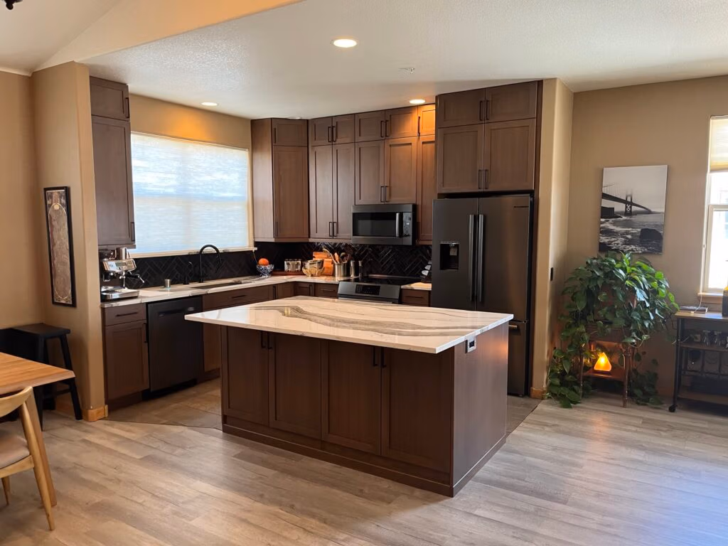 Modern kitchen featuring dark cabinetry, a white marble countertop island, stainless steel appliances, and natural light from large windows, reflecting quality craftsmanship and thoughtful design in home remodeling.